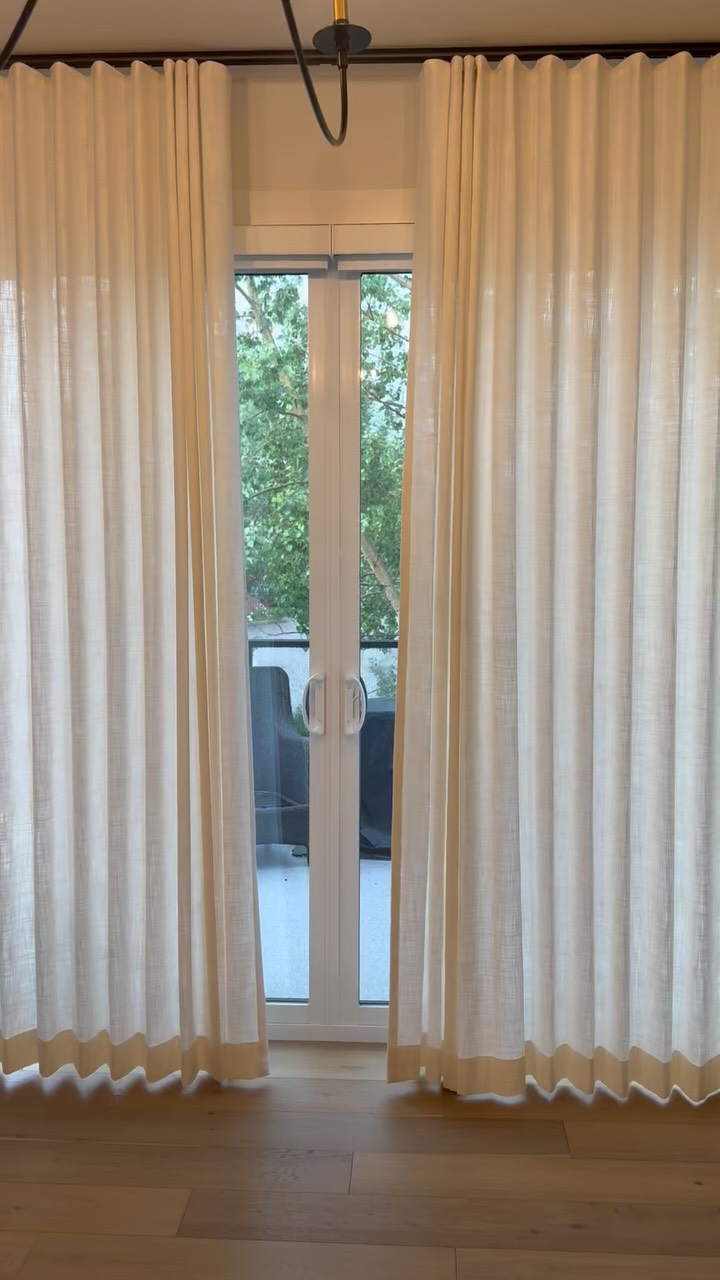 Semi-sheer ripple fold drapes parted at glass patio doors, with green trees outside and light wood flooring