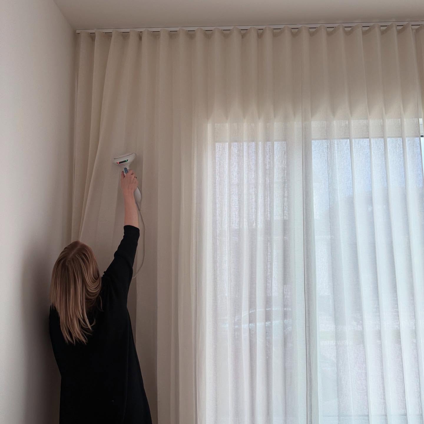 An installer steaming newly hung semi-sheer ripple fold drapery, seen from behind